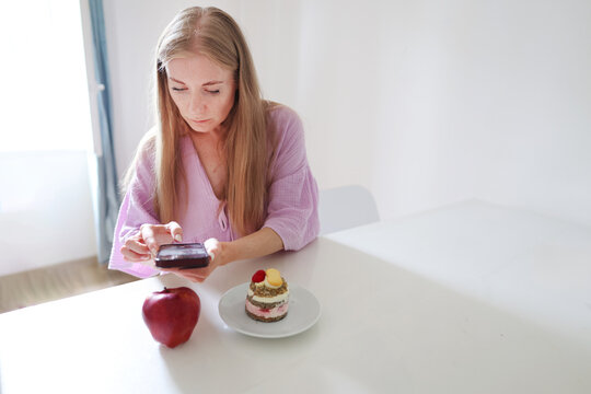 Young woman tracking calories with a mobile app before eating cake, illustrating mindful nutrition and diet planning.