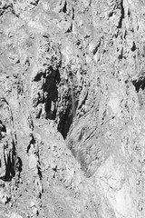 Black and white rugged mountain cliff with narrow waterfall and textured rocky surface for nature backgrounds and adventure themes © Vytenis