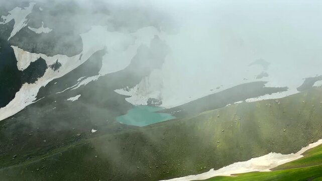 White Abudelauri Lake emerges through dense fog beneath lingering snowfields in Georgias Caucasus, highlighting alpine hydrology, seasonal thaw and remote destination geography for travel media.