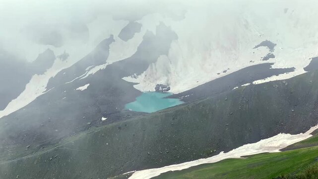 White Abudelauri Lake lies beneath snow-covered slopes and drifting mist in the Caucasus, presenting glacial hydrology, seasonal thaw, remote geography, climate research, and expedition tourism
