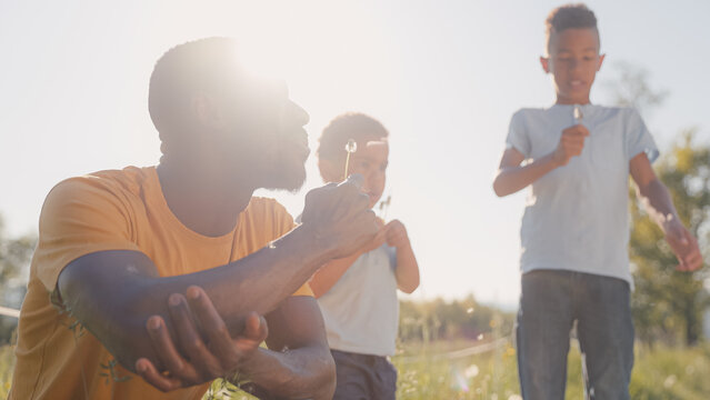 A single father enjoys time with his young sons outdoors in a sunny field during sunset. They laugh and create memories together.