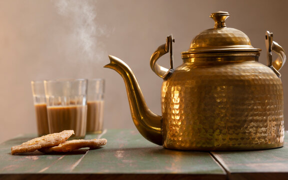 Brass kettle blowing hot air kept next to matthis and three glasses filled with tea on a table