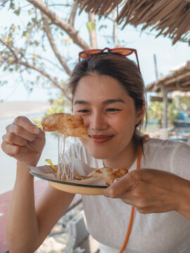 Happy young Asian woman enjoying a delicious cheesy fried pastry, stretching melted cheese outdoors.