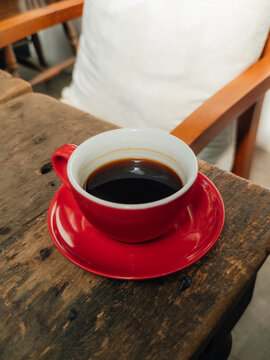 A vibrant red cup filled with hot black coffee sits on a rustic wooden table.