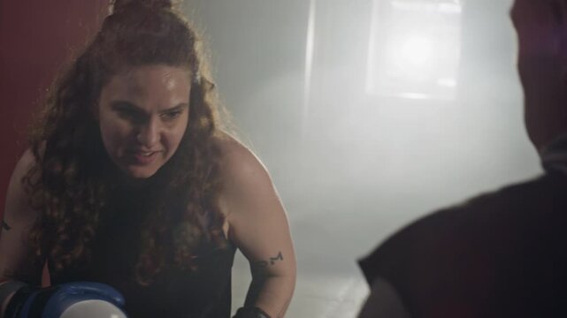 Caucasian young female boxer punching focus mitts held by Caucasian middle aged male trainer in gym. Footage ideal for fitness brand commercials and motivational sports campaigns