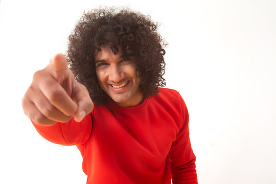 A CURLY HAIRED YOUNG MAN HAPPILY POINTING FINGER TOWARDS CAMERA