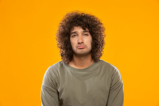 A YOUNG MAN WITH CURLY HAIR LOOKING SAD IN FRONT OF CAMERA