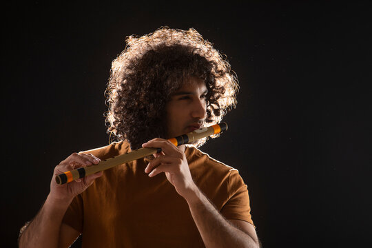 A YOUNG MAN WITH CURLY HAIR STANDING AND PLAYING FLUTE