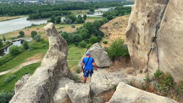 Man walking among Uplistsikhe ruins above the Kura River in Georgia explores rock-cut urban history, supporting archaeological tourism, destination marketing and educational heritage programs.