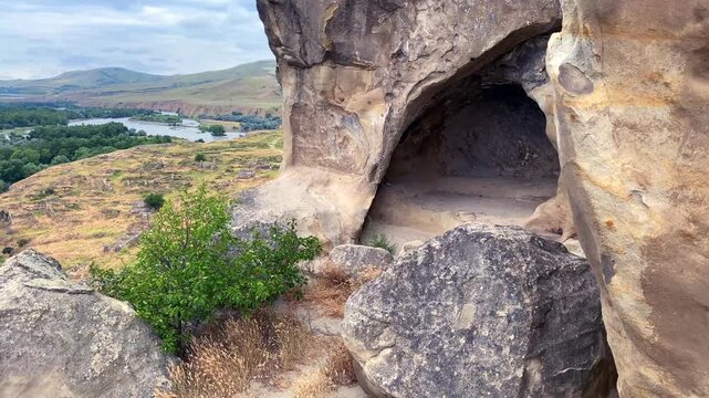 A tourist walks between massive sandstone blocks and carved chambers at Uplistsikhe, representing self-guided heritage travel, archaeological education and access to Georgia's ancient urban landscape