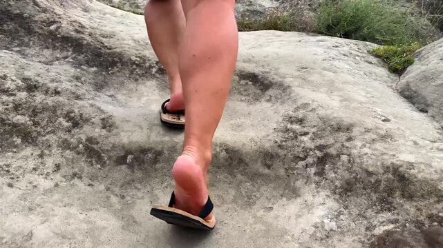 A tourist climbs hand-carved stone steps at Uplistsikhe in sandals, connecting active travel, physical effort, historic infrastructure and visitor access within Georgia's ancient cave settlement.