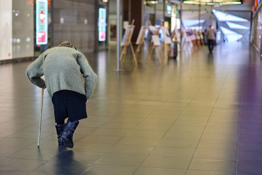 Bent elderly woman, walking stick. View from behind, frail, old age. Loneliness, poverty, struggle. Social issue, oldman care, and support needs
