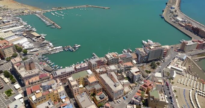 Aerial view of the harbor of Anzio, located in province of Rome, Italy. Panorama from above of a coastal town with vibrant waters, surrounding piers, docks filled with boats in a sunny summer morning.