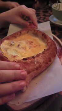 Enjoying a steaming adjarian khachapuri, a delicious cheese-filled bread, topped with a rich egg. Experience the joy of sharing this traditional Georgian dish in a warm cafe.
