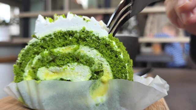 Watch as a vibrant green roll cake is carefully sliced, revealing its creamy layers inside. This delightful treat is prepared in a charming cafe, perfect for dessert lovers.