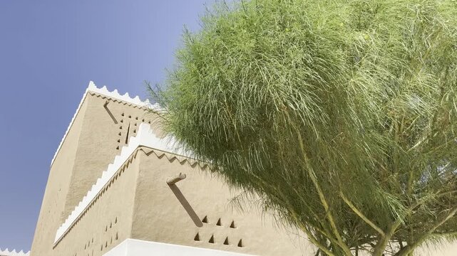 Low angle view of modern traditional Najdi architecture building with mudbrick pattern and green tree