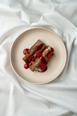 A plate holds a dessert featuring layers of chocolate sauce and fresh raspberries. The setting is...