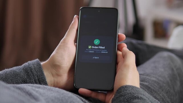 Person uses a smartphone trading platform to manage risk, exit a position and confirm a completed market order amid uncertain financial conditions.