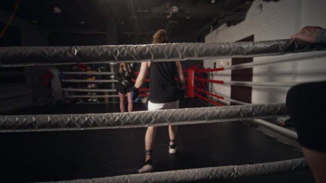 Young Caucasian female boxer entering ring under ropes held by middle-aged Caucasian male coach. Footage suitable for fitness center marketing and athletic training commercials