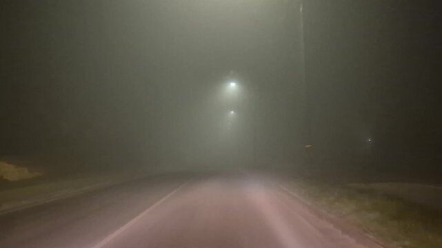 Night driving journey along a quiet suburban road enveloped in dense thick fog. First-person dashboard camera shot.