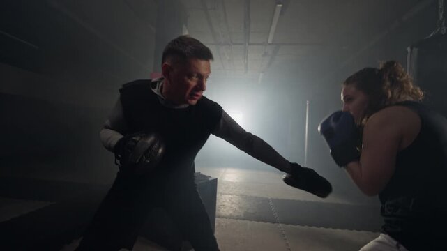 Young Caucasian woman boxing with middle aged Caucasian male trainer holding focus mitts in gym. Clip is perfect for fitness brand advertising and gym marketing campaigns