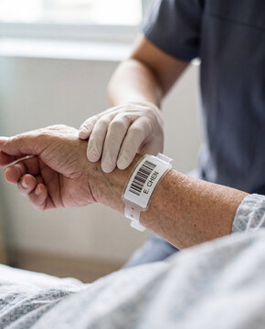 Nurse holding patient's hand with hospital identification wristband in clinical setting