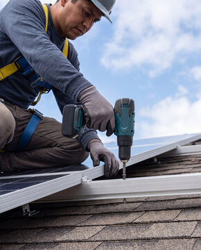 Solar panel installer using cordless drill to fasten mounting rail on shingled roof
