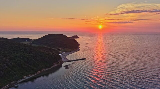 High-angle drone footage capturing a lush green pine forest meeting the crystal-clear turquoise waters of a secluded bay cape of Rodon(Kepi Rodonit), on beatiful sunset