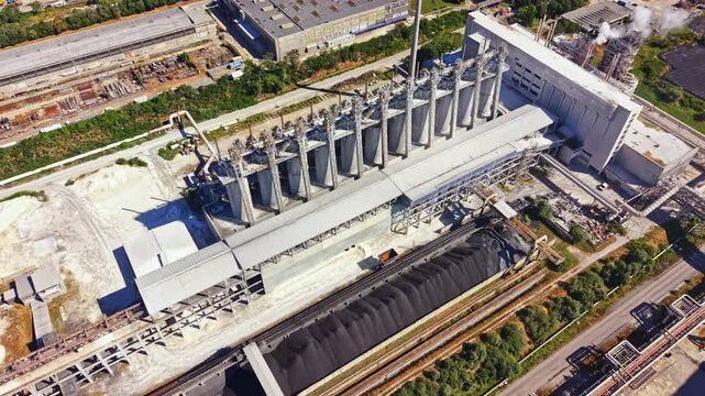 Aerial view of an industrial area featuring several silos and machinery. The location has a railway track running nearby. This is in a working environment during daylight hours.