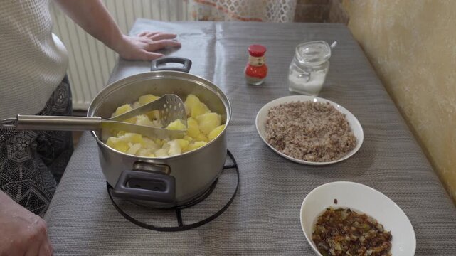 Close up of mashing hot boiled potatoes with steam rising from the pot, Preparing homemade mashed potatoes in a stainless steel saucepan