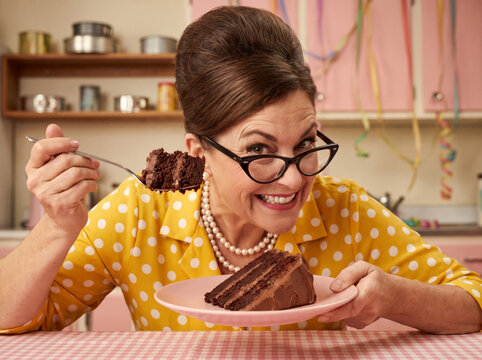 Retro woman mischievously eating chocolate cake in a vintage pink kitchen, perfect for comedic food advertising and bakery branding.