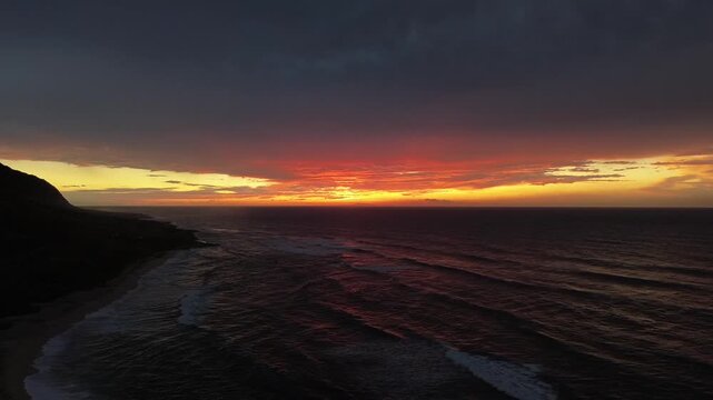 Drone view of sunset over coastline at St Abbs Head, capturing dramatic clouds, ocean waves, glowing horizon, and colorful evening sky above rugged coast