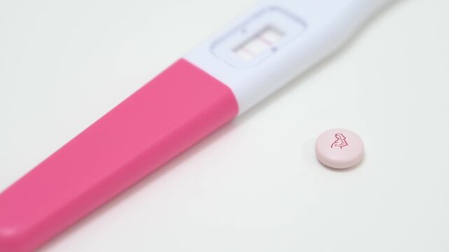 A positive rapid pregnancy test next to a pink prenatal medication pill
