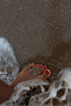 Vertical top view of dark skinned foot touched by sea wave