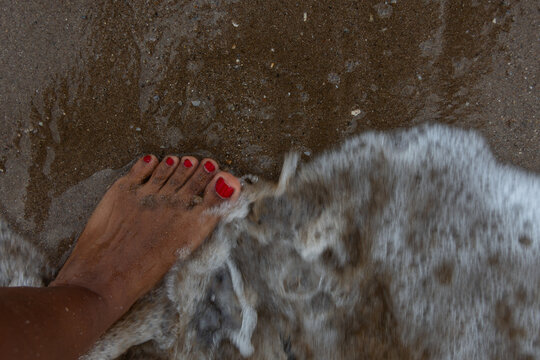 Top view of dark skinned foot touched by sea wave on beach