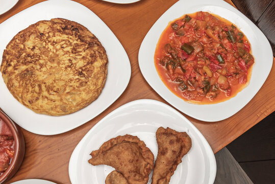 Spanish Tapas Trio: Whole Tortilla Espa&ntilde;ola, Vegetable Stew, and Fried Empanadillas on White Plates