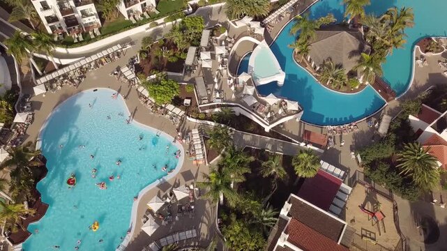 Aerial view of luxury tropical resort swimming pools with people relaxing and swimming in clear blue water.