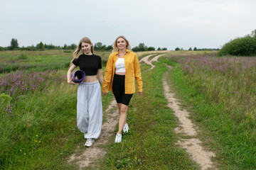 Two women mother and adult daughter walking along a grassy rural path holding hands in a field
