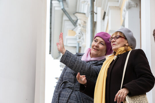 Two elderly friends talk and gesticulate while standing near a building in the city on a cool early spring day.