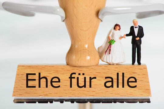 Ein Holzstempel ist beschriftet mit dem Aufdruck:  Ehe f&uuml;r alle und ein Hochzeitspaar als Modellfigur