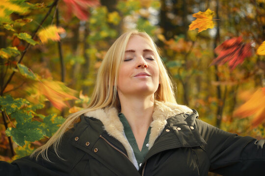 Beautiful young woman in a park enjoying the autumn air, sunshine and falling colorful leaves