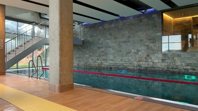 A serene indoor lap pool with a stone wall and clear glass sauna view, reflecting a tranquil atmosphere perfect for luxury spa relaxation, wellness retreats, and athletic training