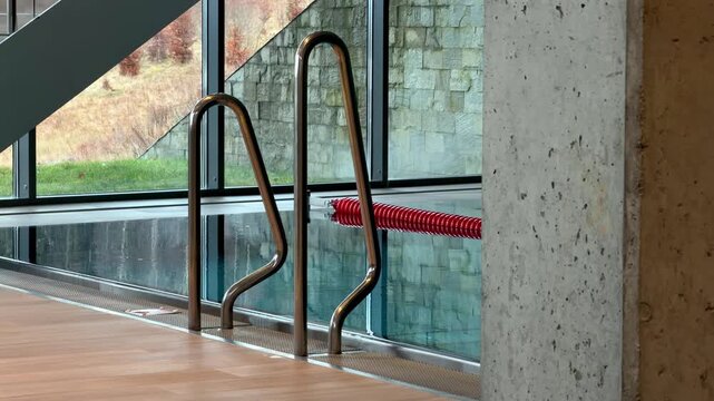 A stainless steel pool ladder sits by the water edge in a luxurious indoor swimming facility, conveying a serene atmosphere for athletic training or quiet relaxation in nature
