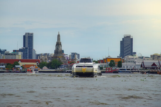 Bangkok, Thailand - June  16, 2026 : An electric passenger boat traveling on the Chao Phraya River passes the prang of Wat Arun, a beautiful viewpoint and a symbol of Bangkok.