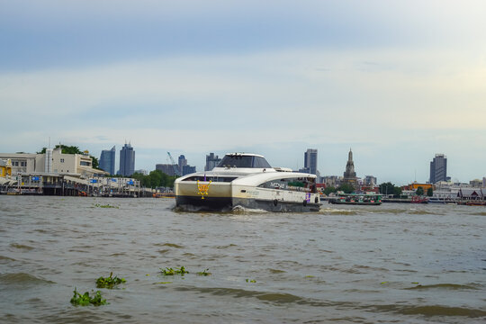 Bangkok, Thailand - June  16, 2026 : An electric passenger boat traveling on the Chao Phraya River passes the prang of Wat Arun, a beautiful viewpoint and a symbol of Bangkok.