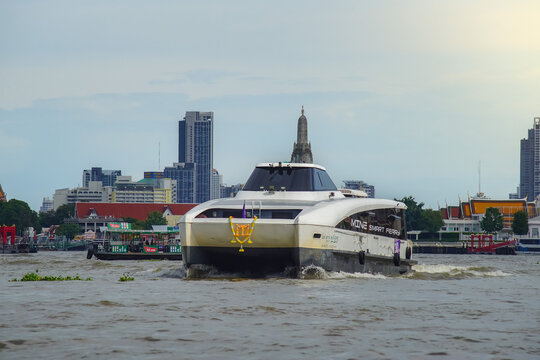 Bangkok, Thailand - June  16, 2026 : An electric passenger boat traveling on the Chao Phraya River passes the prang of Wat Arun, a beautiful viewpoint and a symbol of Bangkok.