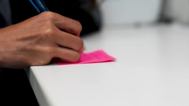Taking notes with pen on pink sticky note