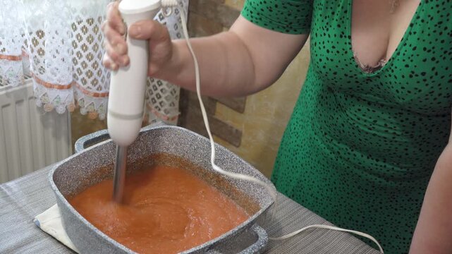 Process of blending hot sauce in a granite pot on the table, Woman mashing vegetable soup with a hand immersion blender close up