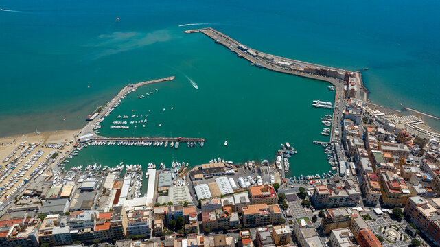Aerial view of the harbor of Anzio, located in province of Rome, Italy. Panorama from above of a coastal town with vibrant waters, surrounding piers, docks filled with boats in a sunny summer morning.