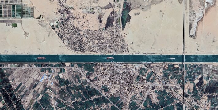 Aerial view of the Suez Canal cutting through a dense urban grid in Ismailia Egypt with container ships passing between residential blocks.